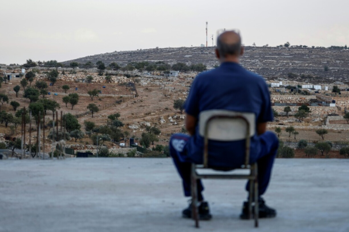 A Palestinian man sits on the rooftop of his house as he looks at a newly established Israeli settler outpost in Burqah in the Israeli-occupied West Bank