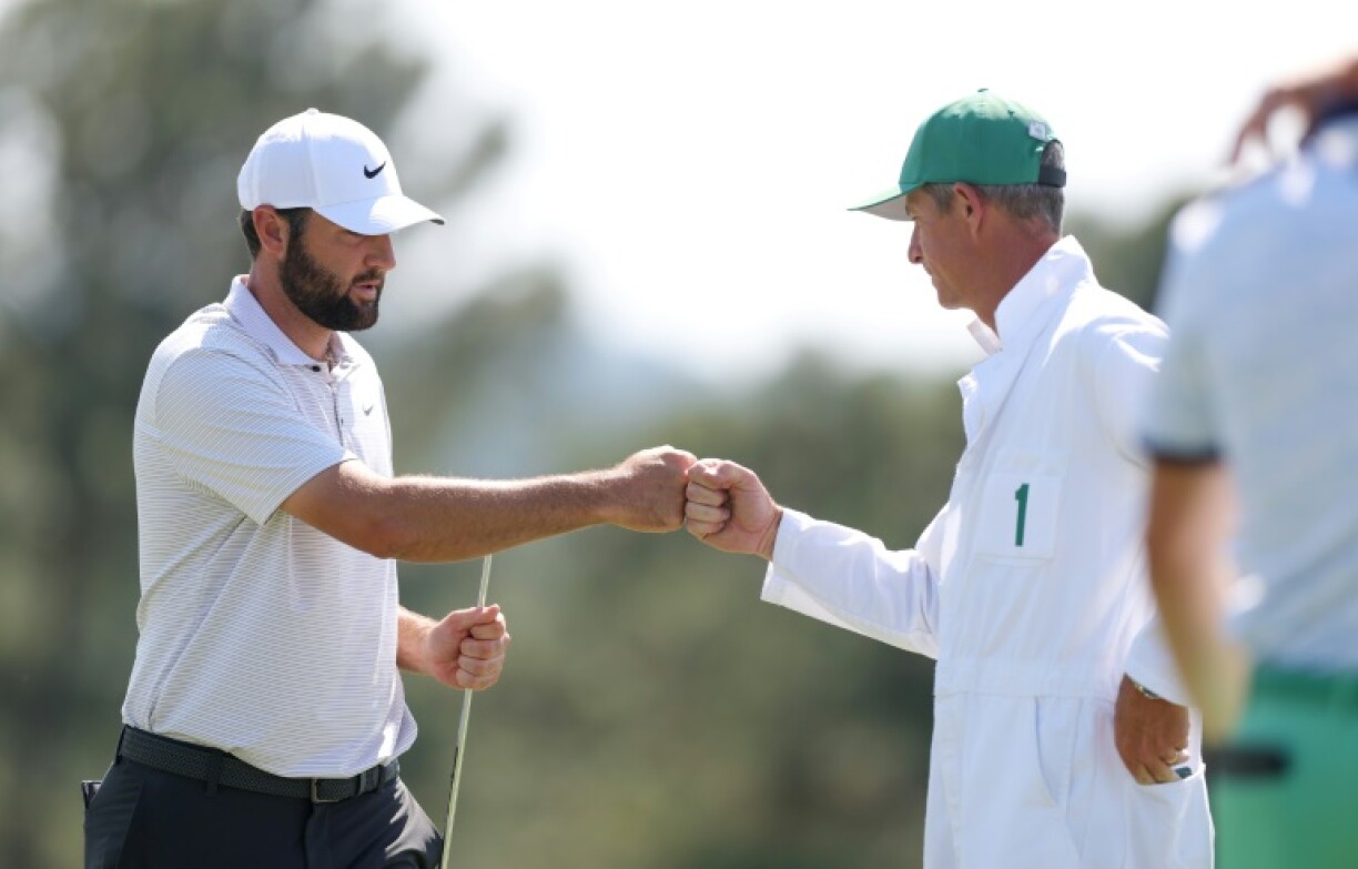 Top-ranked defending champion Scottie Scheffler, left, bumps fists with caddie Ted Scott on the 18th green after firing a 68 in the opening round of the 89th Masters at Augusta National
