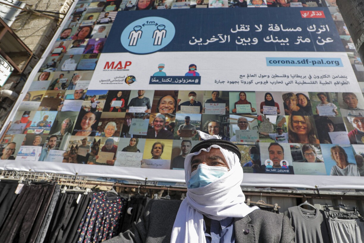 An elderly Palestinian, clad in mask due to the COVID-19 coronavirus pandemic, stands before an information billboard asking people to distance at least one metre apart from each other as a pandemic precaution, in the city centre of the flashpoint city of Hebron in the occupied West Bank on February 21, 2020.
