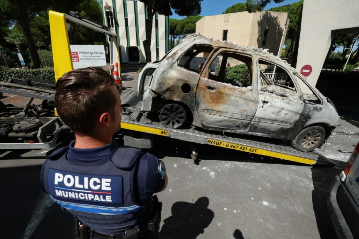 Un policier devant une voiture brûlée placée sur la plateforme d'un véhicule de remorquage à La Grande Motte, deux jours après l'attentat contre une synagogue, le 26 août 2024 dans l'Hérault