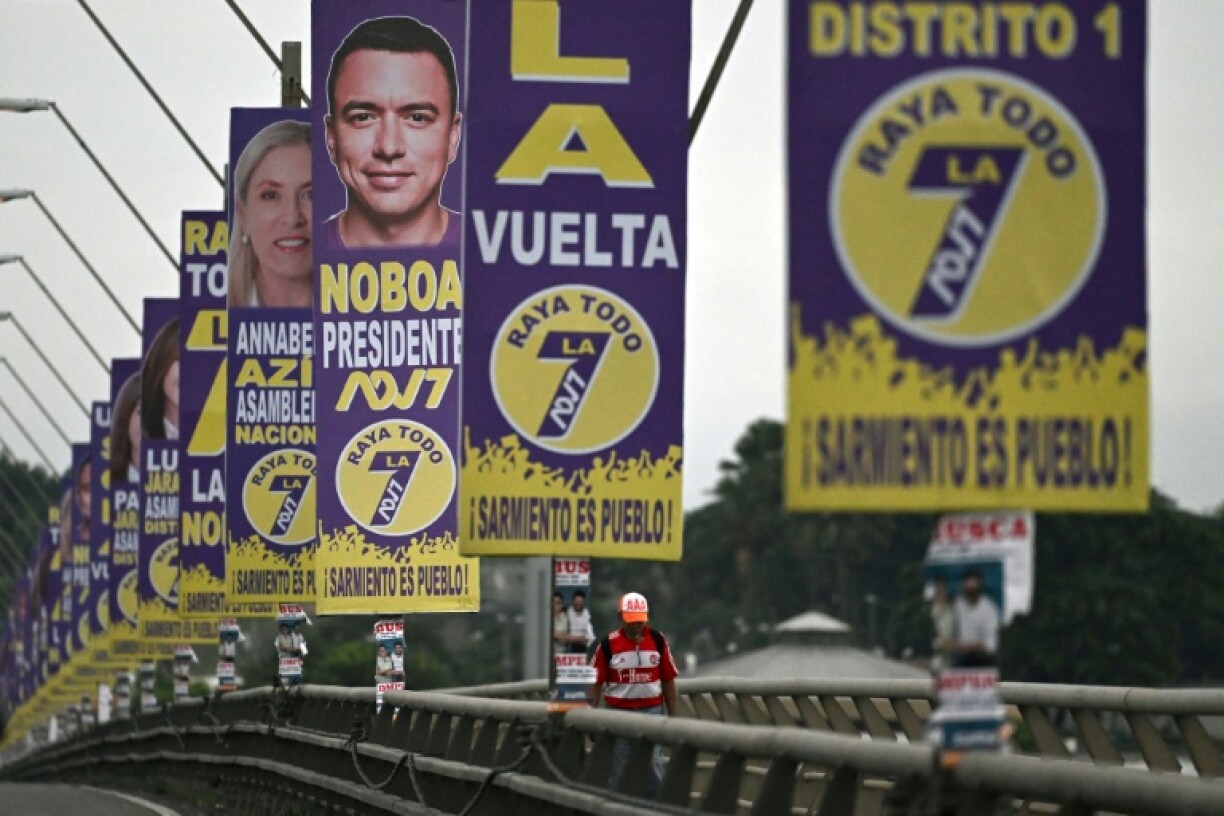 A man walks on a bridge decorated with campaign posters for President Daniel Noboa