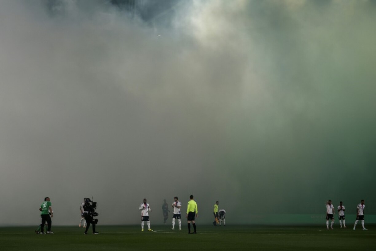 Lyon players stand shrouded in smoke created by flares prior to the start of their Ligue 1 match at fierce rivals Saint-Etienne