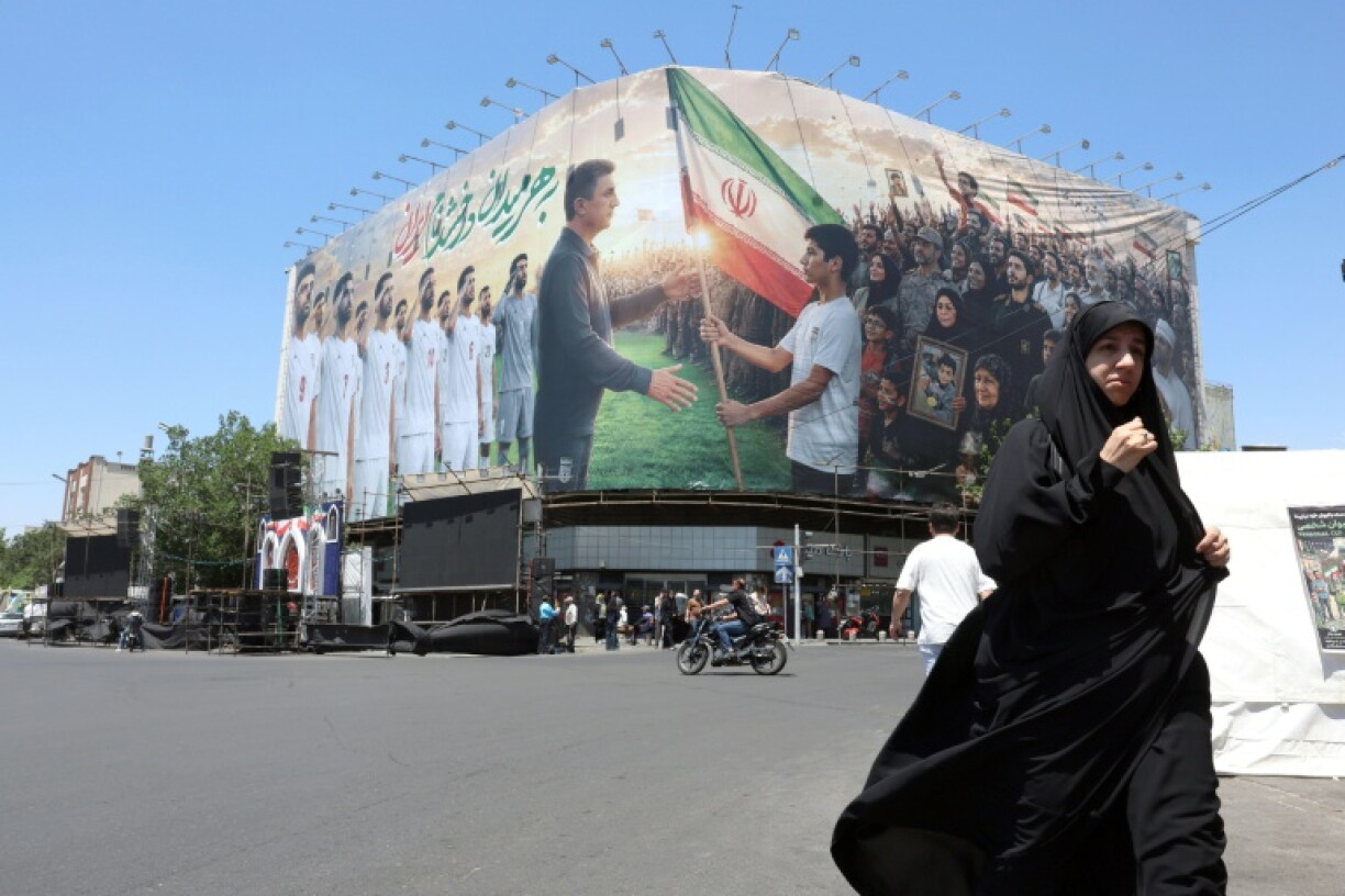 Une Iranienne passe devant un panneau d'affichage géant mettant en scène l'équipe nationale iranienne de football qui a pris la direction de la Turquie pour y préparer le Mondial-2026, le 18 mai 2026 à Téhéran