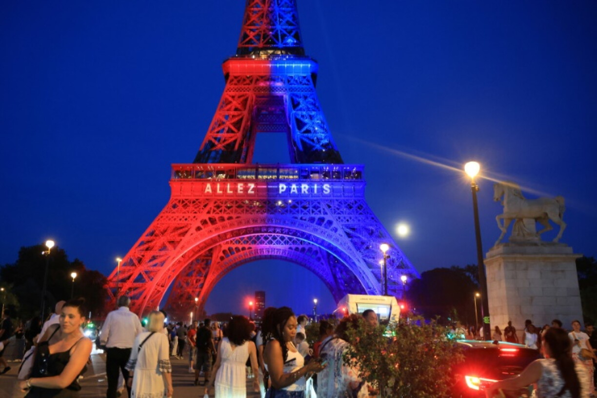 Des passants déambulent sous la Tour Eiffel, illuminée aux couleurs du Paris Saint-Germain (PSG) et sur laquelle est inscti le message