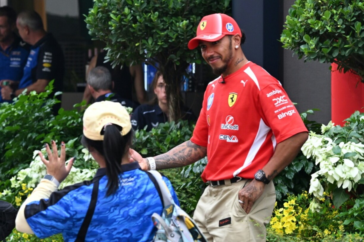 Ferrari's British driver Lewis Hamilton (R) smiles as he arrives at the paddock ahead of the Singapore Formula One Grand Prix