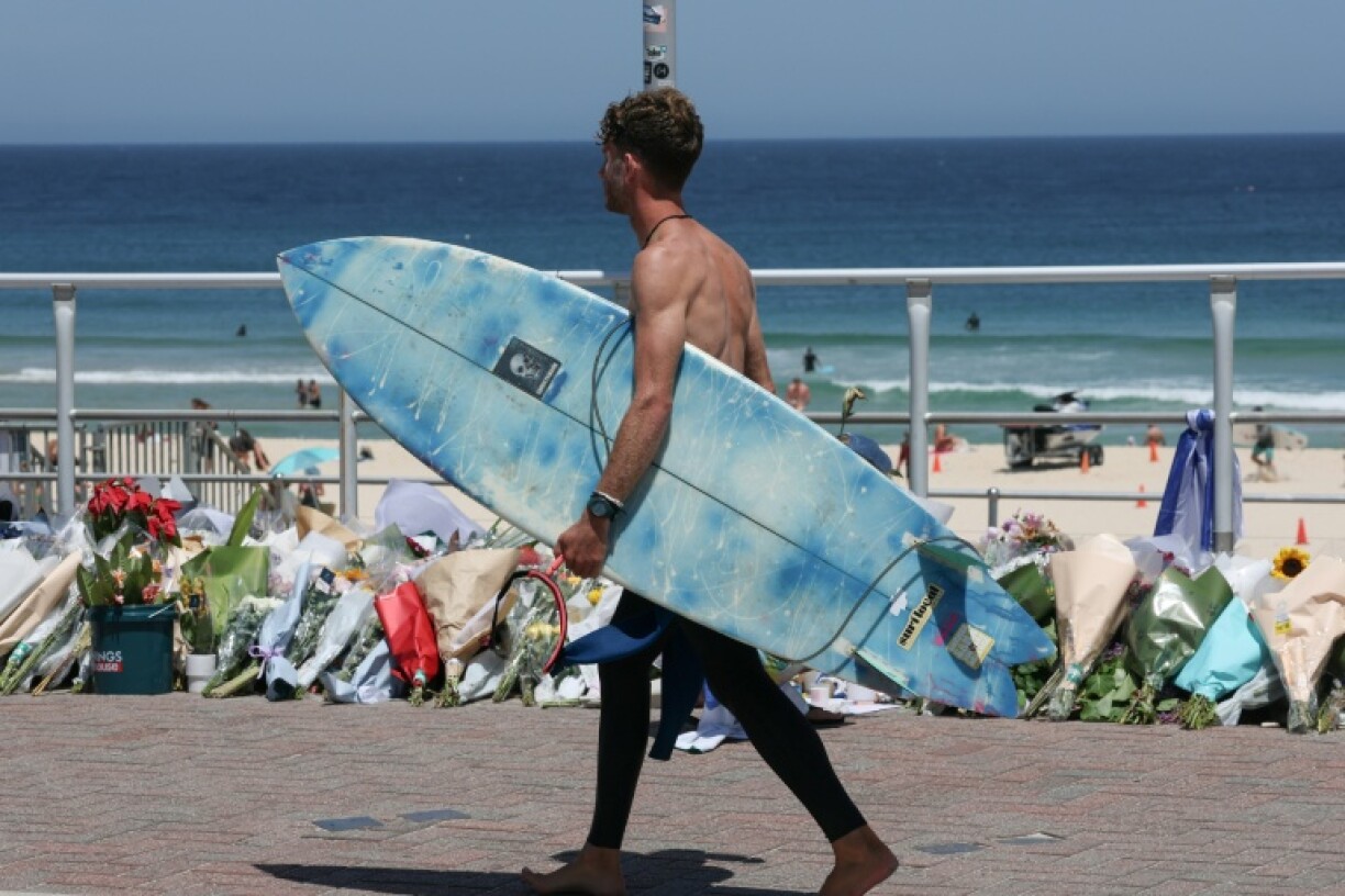 Un surfeur passe devant les fleurs déposées sur la promenade de la plage de Bondi à Sydney, le 18 décembre 2025, en hommage aux victimes de l'attentat du 14 décembre