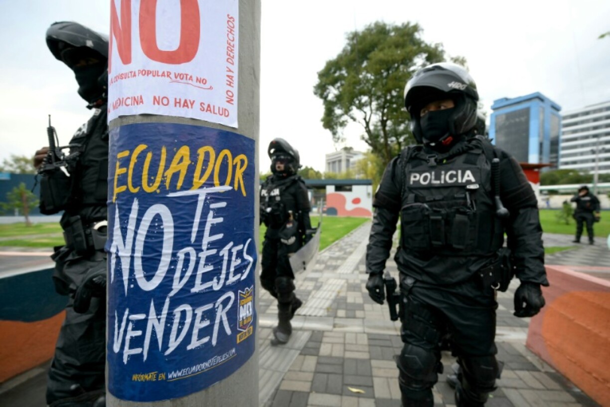 Ecuadoran police officers in Quito walk past a flyer for a 'No' vote ahead of the referendum on foreign military bases