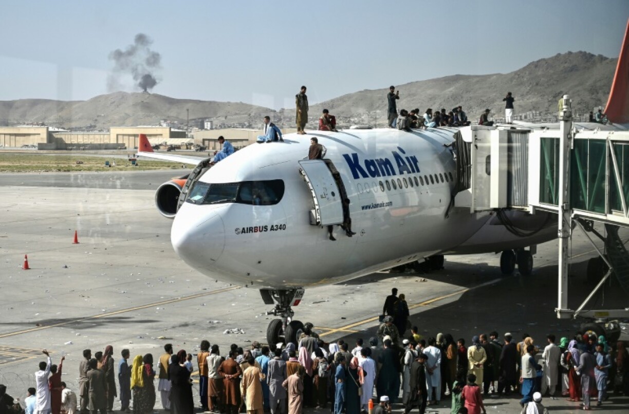 Afghan people climb atop a plane as they wait at the Kabul airport on August 16, 2021, in the rush to leave the country as the Taliban took over