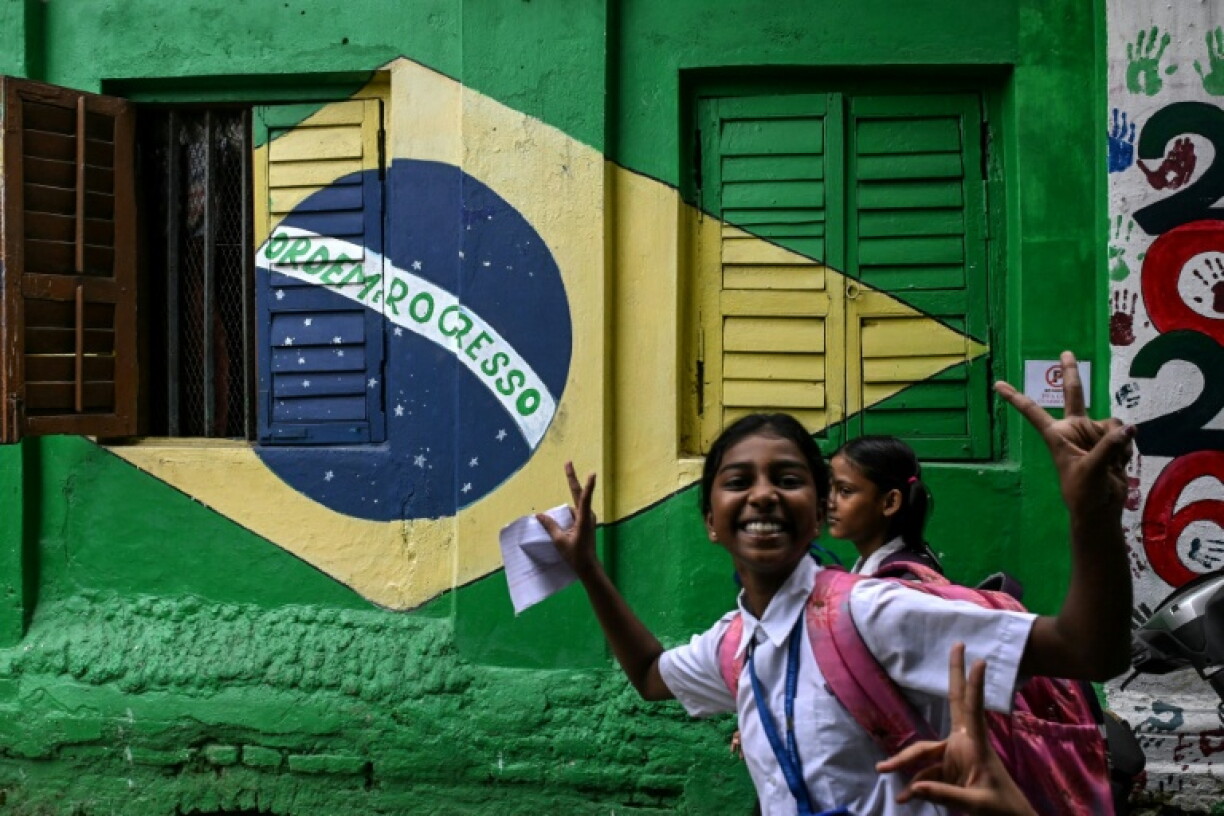 Students react as they walk past graffiti featuring the Brazilian national flag ahead of the friendly football match between India and Brazil in Kolkata