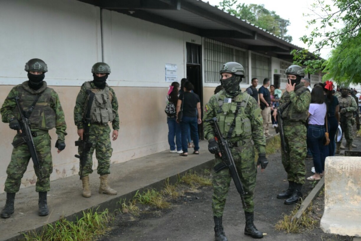 Military personnel stand guard as people queue to vote at a polling station
