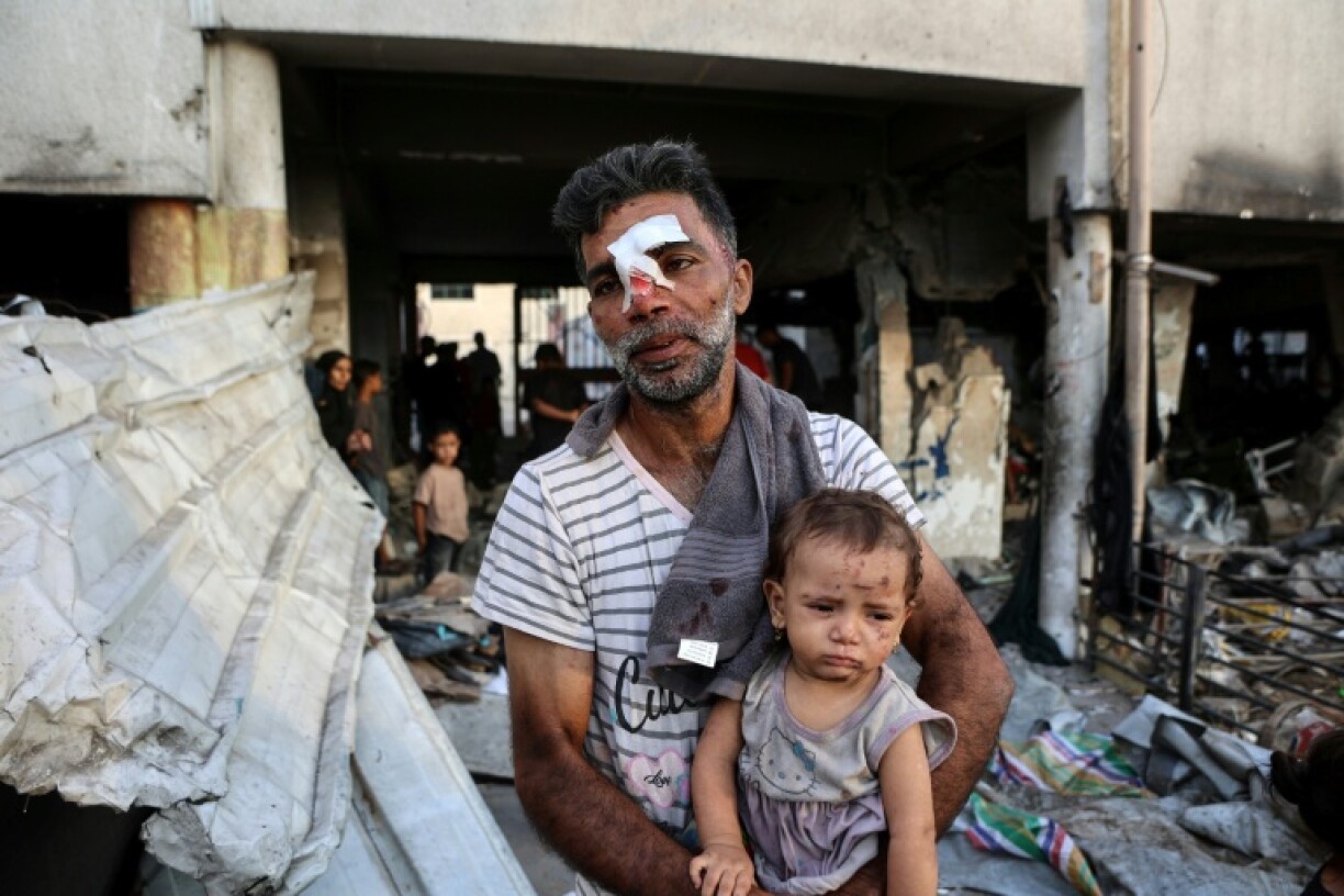 An injured man carries a toddler after a school in Gaza City being used to shelter displaced Palestinians was hit by an Israeli strike
