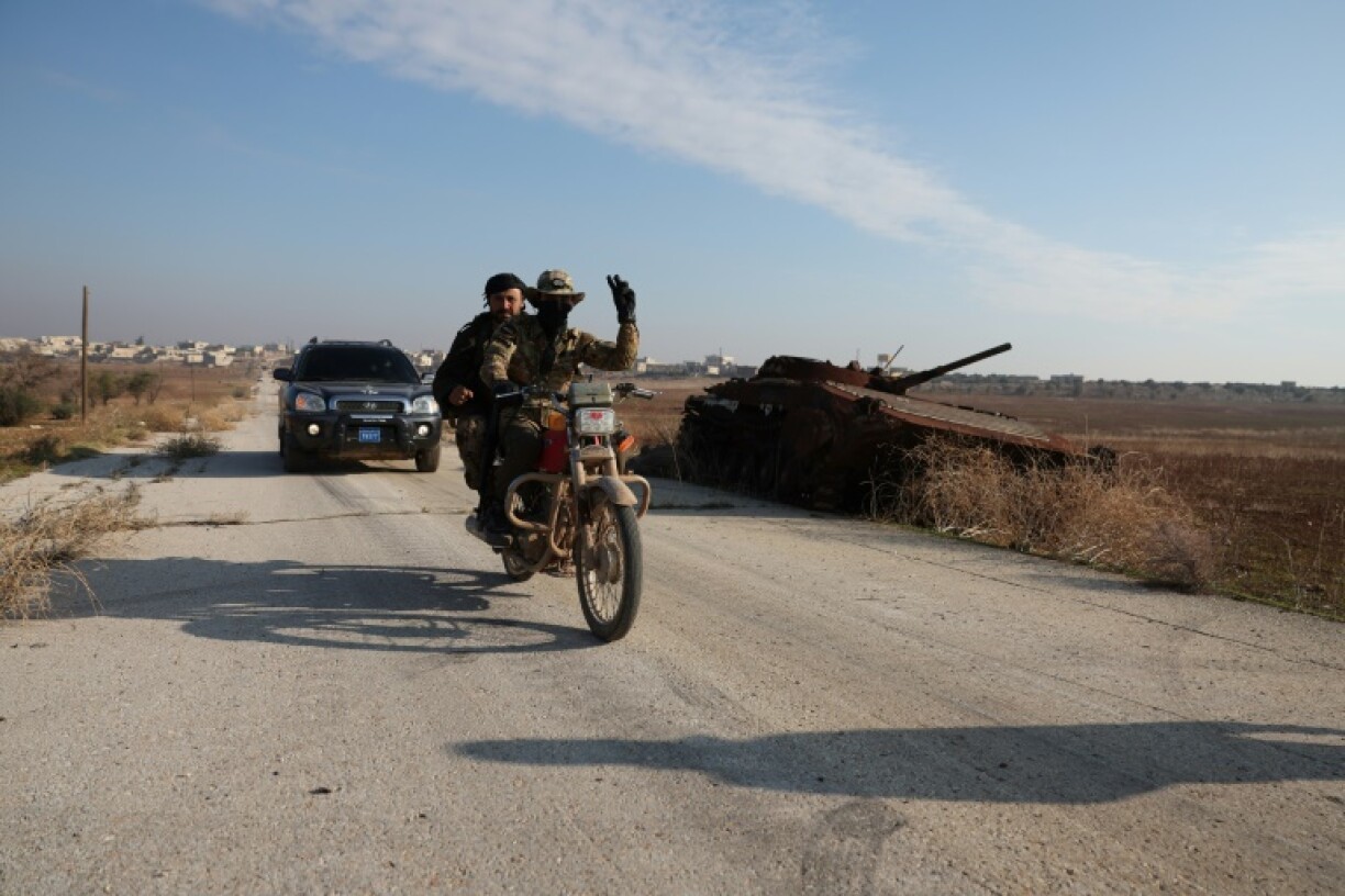 Fighters pass a damaged Syrian Army tank in Miznaz, Syria, which was taken over by jihadists and their Turkish-backed allies in battles with government forces in Aleppo province