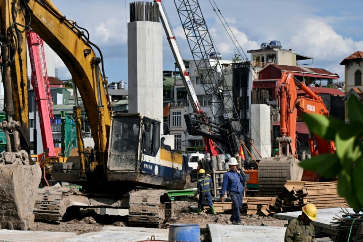Workers walk past excavators at the construction site of the Tran Hung Dao Bridge, spanning the Red River