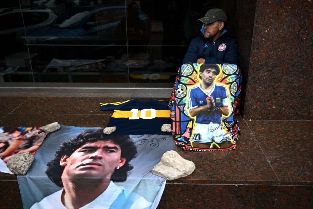 A supporter of Argentine football legend Diego Maradona sits beside portraits and memorabilia outside the courthouse during the final hearing of defense closing arguments in the trial over Maradona's 2020 death