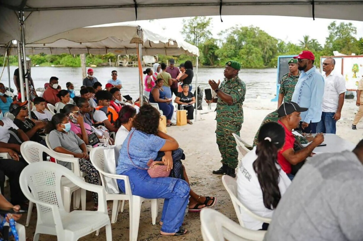 Guyana's President Irfaan Ali (R, red cap) and military staff hold a meeting with survivors and relatives of those missing since the capsizing of a ferry that left at least 41 people dead