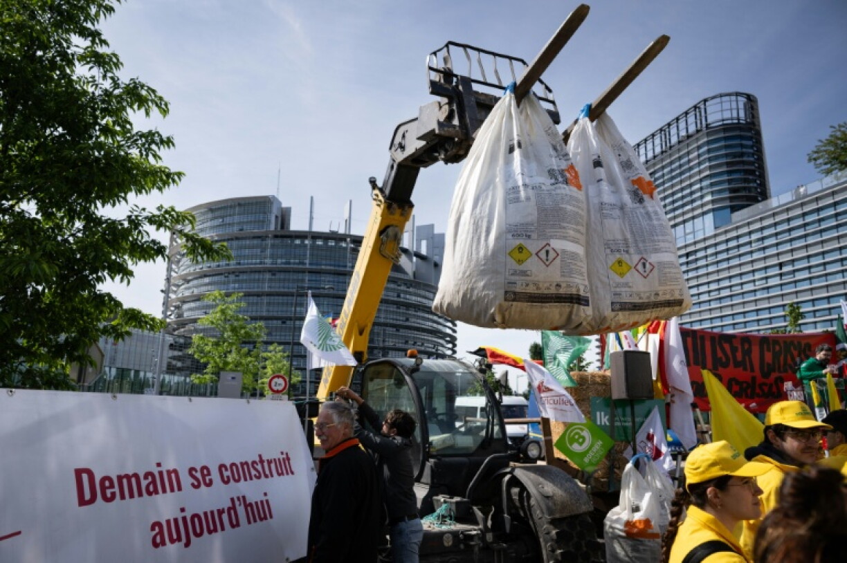 Des agriculteurs suspendent des sacs d'engrais à un tracteur lors d'une manifestation devant le Parlement européen à Strasbourg, le 19 mai 2026