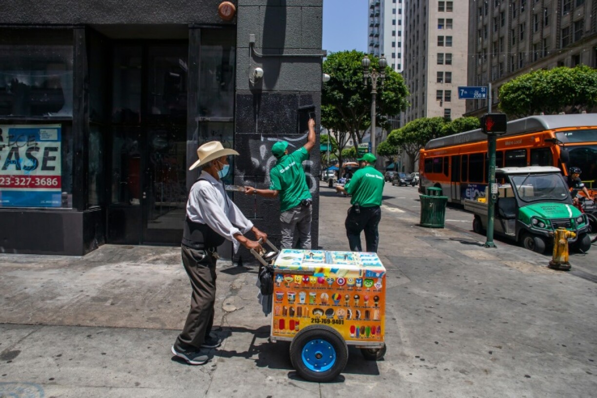 An ice cream vendor walks past workers cleaning graffiti in downtown Los Angeles left by the protesters