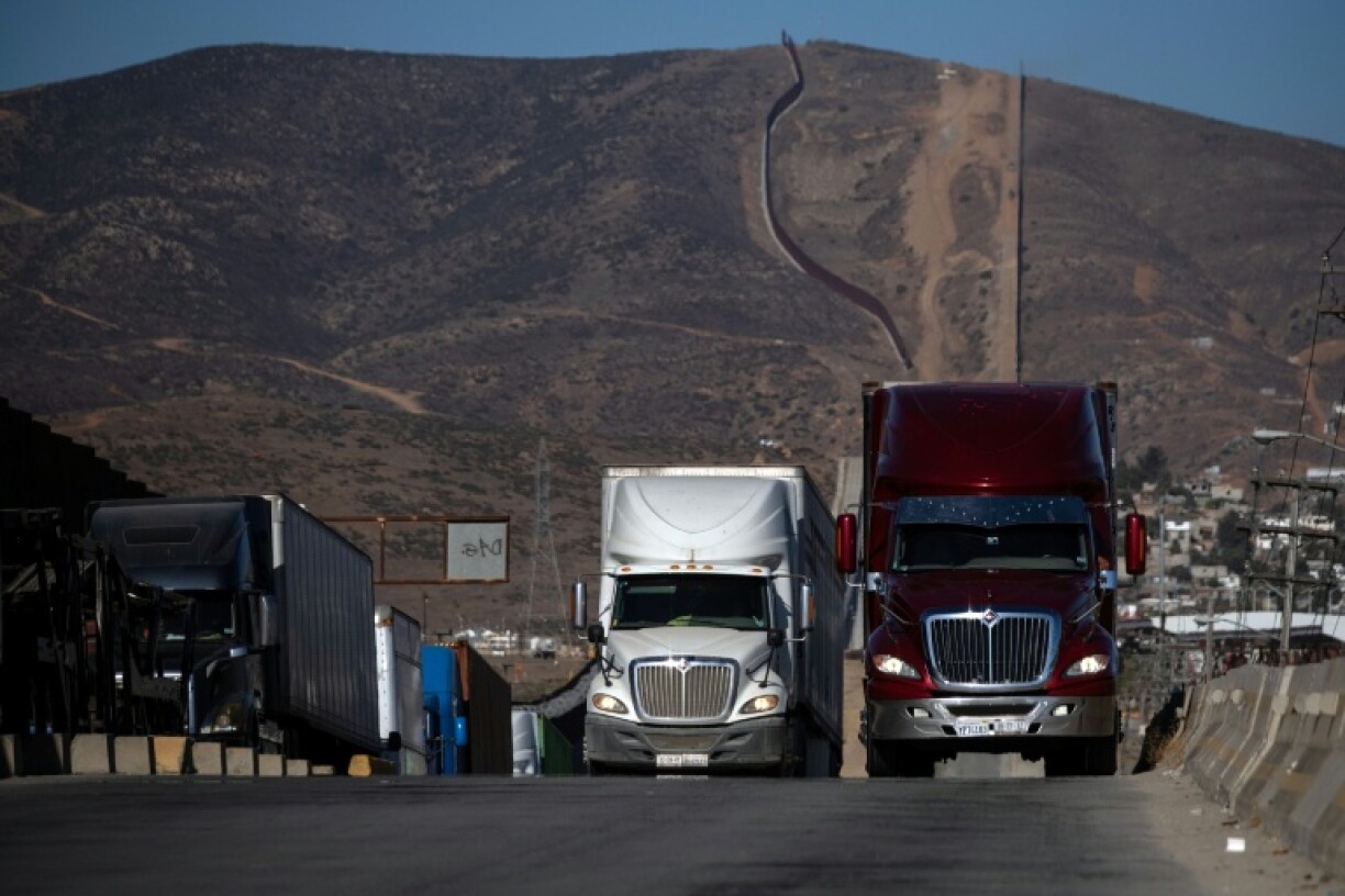 Cargo trucks queue next to the border wall before crossing into Tijuana, Mexico