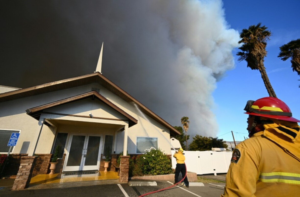 Private firefighters protect a church as the plume of smoke from the Hughes fire darkens the sky in Castaic, a northwestern part of Los Angeles, California, on January 22, 2025