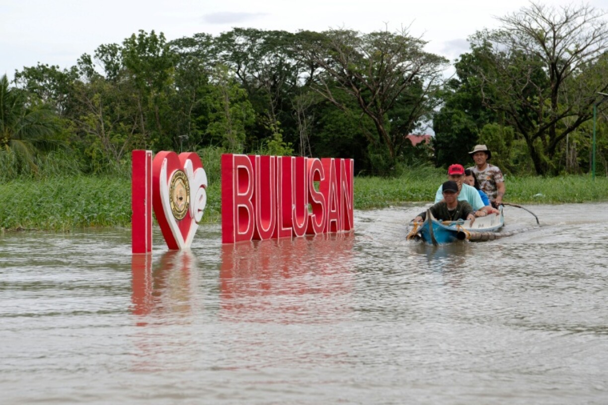 Residents ride in a wooden boat past a submerged sign in Bulacan province, north of Manila on Friday