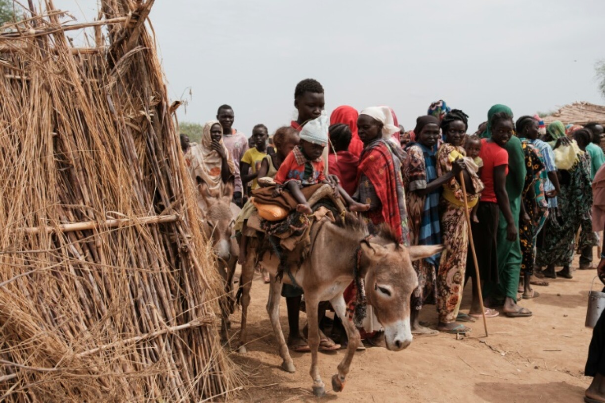 Ali Abdula, 16, guides his donkey carrying two younger siblings, both suffering from malnutrition, past internally displaced people lining up to register for aid in Agari, in Sudan's South Kordofan state, on June 17, 2024