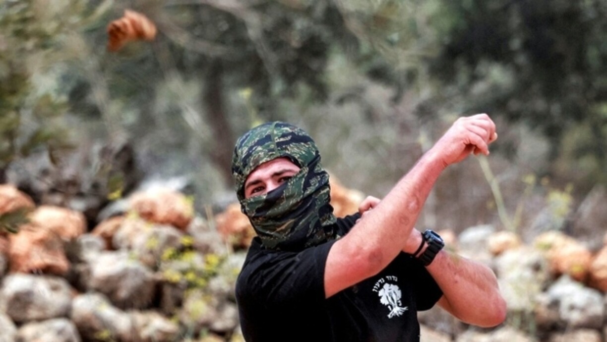 Un homme masqué lance des pierres sur des Palestiniens rassemblés pour la saison annuelle de la récolte des olives, lors d'une attaque de colons israéliens sur le village palestinien de Beita, au sud de Naplouse, en Cisjordanie occupée