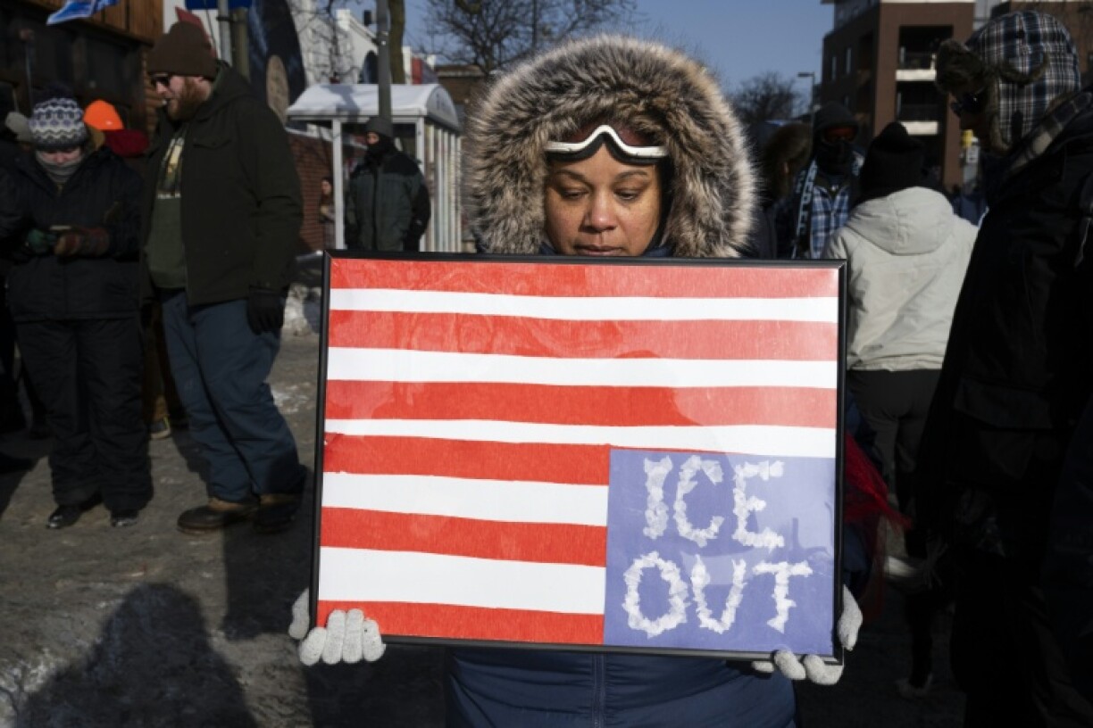 Une femme tient une pancarte ornée d'un drapeau américain à l'envers devant un mémorial improvisé à l'endroit où Alex Pretti a été abattu la veille par la police de l'immigration (ICE) à Minneapolis, dans le Minnesota, le 25 janvier 2026