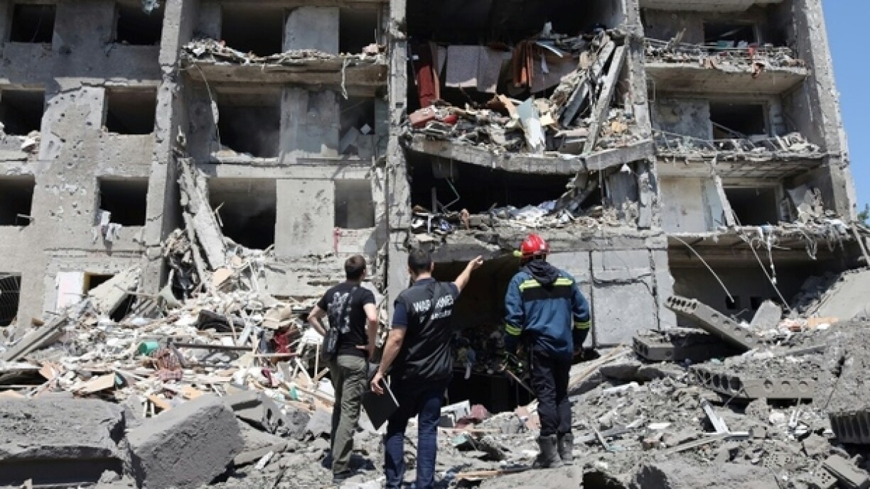 A Serguiïvka, dans le sud de l'Ukraine, un enquêteur, un civil et un sauveteur, le 1er juillet 2022, devant un immeuble détruit par une frappe de missile russe