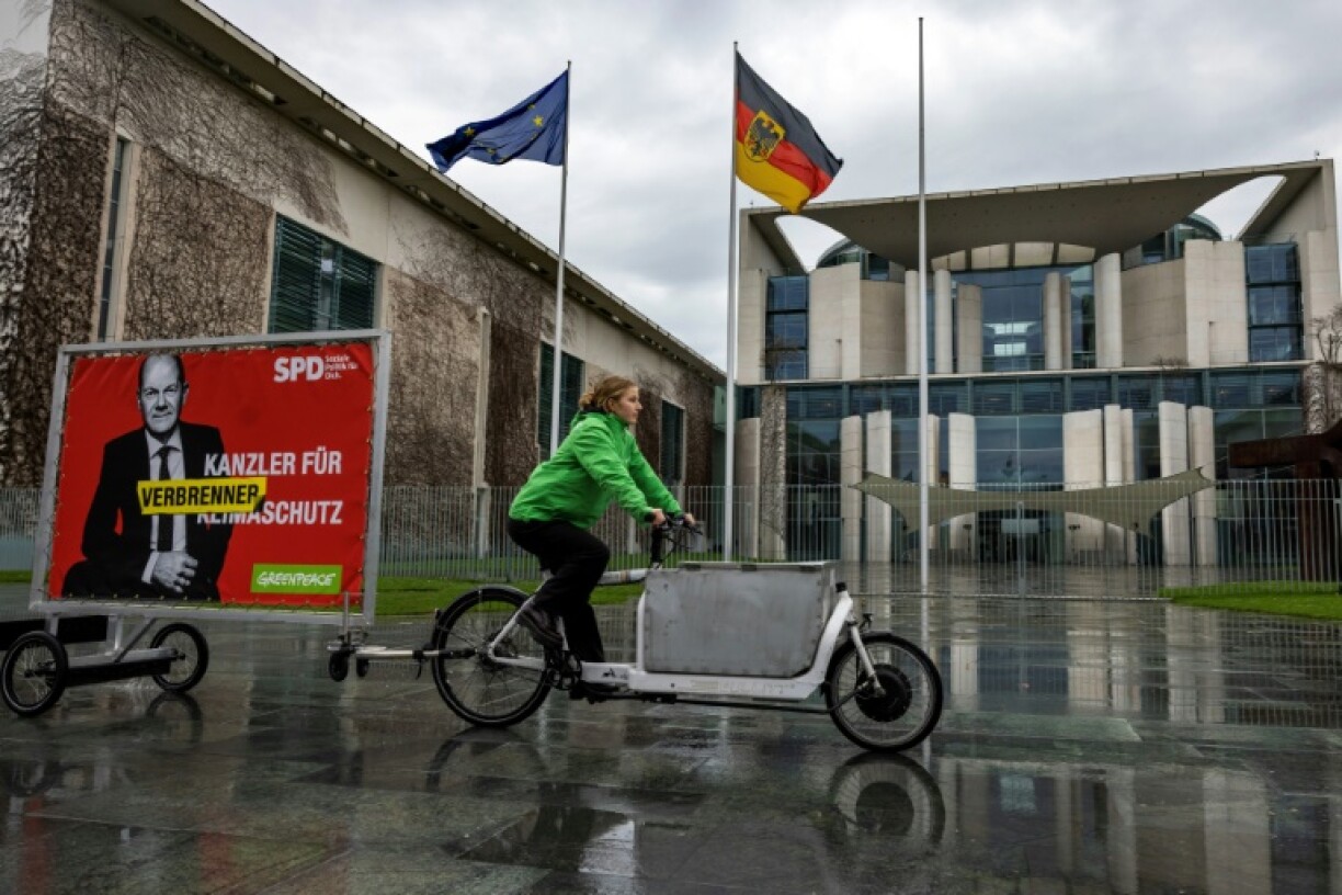 Un manifestant de Greenpeace à vélo passe devant la chancellerie à Berlin en tirant un portrait du chancelier allemand Olaf Scholz avec les mots
