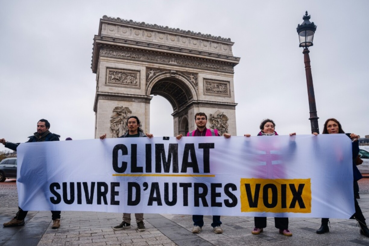 Des militants pour le climat brandissent une banderole devant l'Arc de triomphe à Paris le 12 décembre 2025