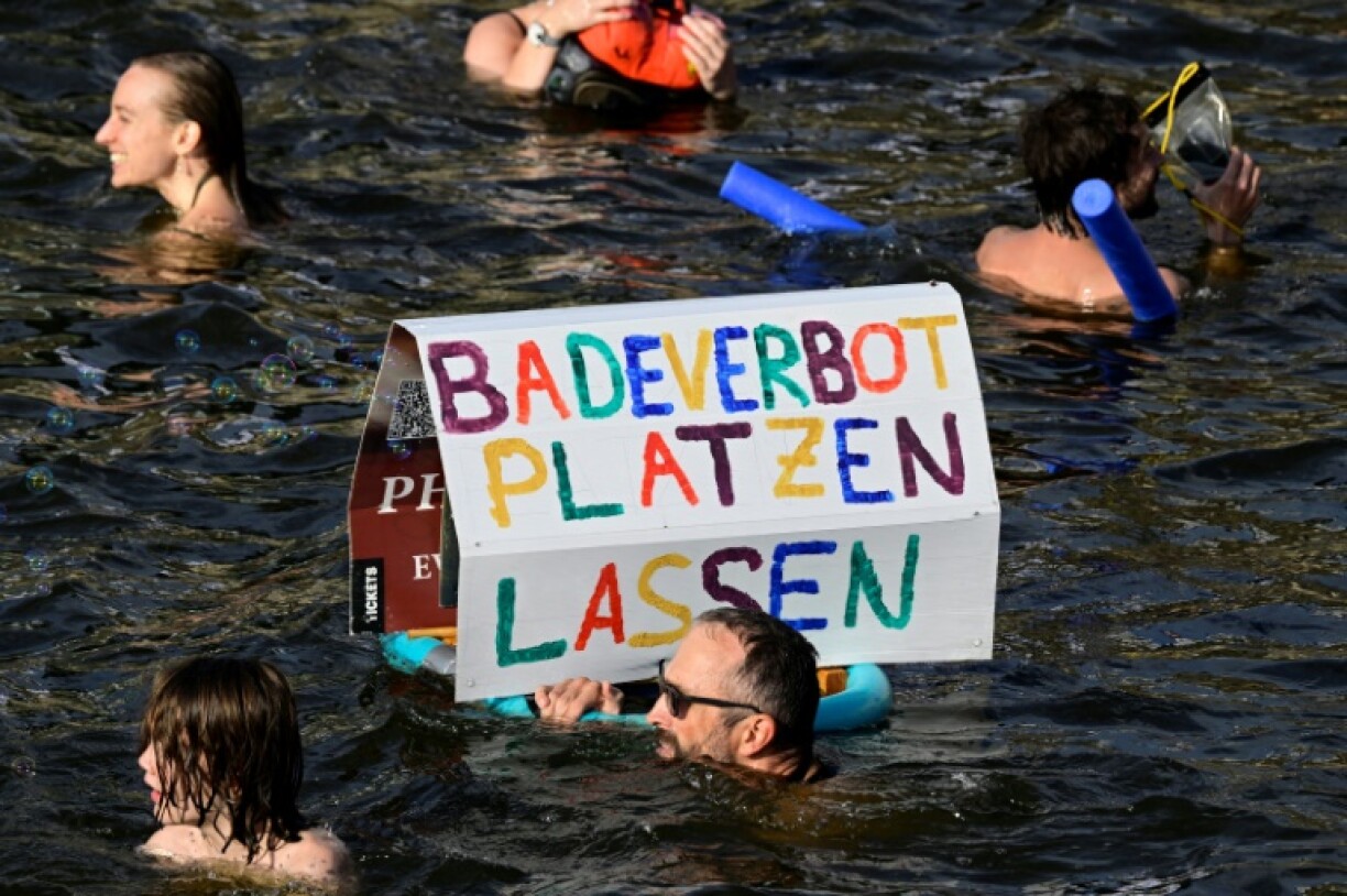 A participant swims with a placard with the slogan 'Let the bathing ban fall' while taking a dip in the Spree river during a swimming demonstration for the abolition of the general swimming ban in the inner-city Spree river in central Berlin on August 12, 2025.