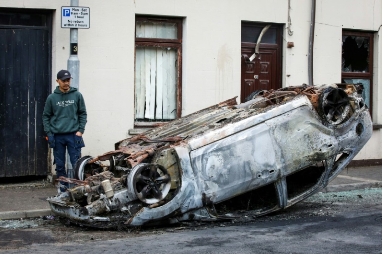 Un passant observe les restes d'une voiture calcinée, au lendemain d'une nouvelle nuit d'émeutes visant des immigrés, le 11 juin 2025 à Ballymena, en Irlande du Nord