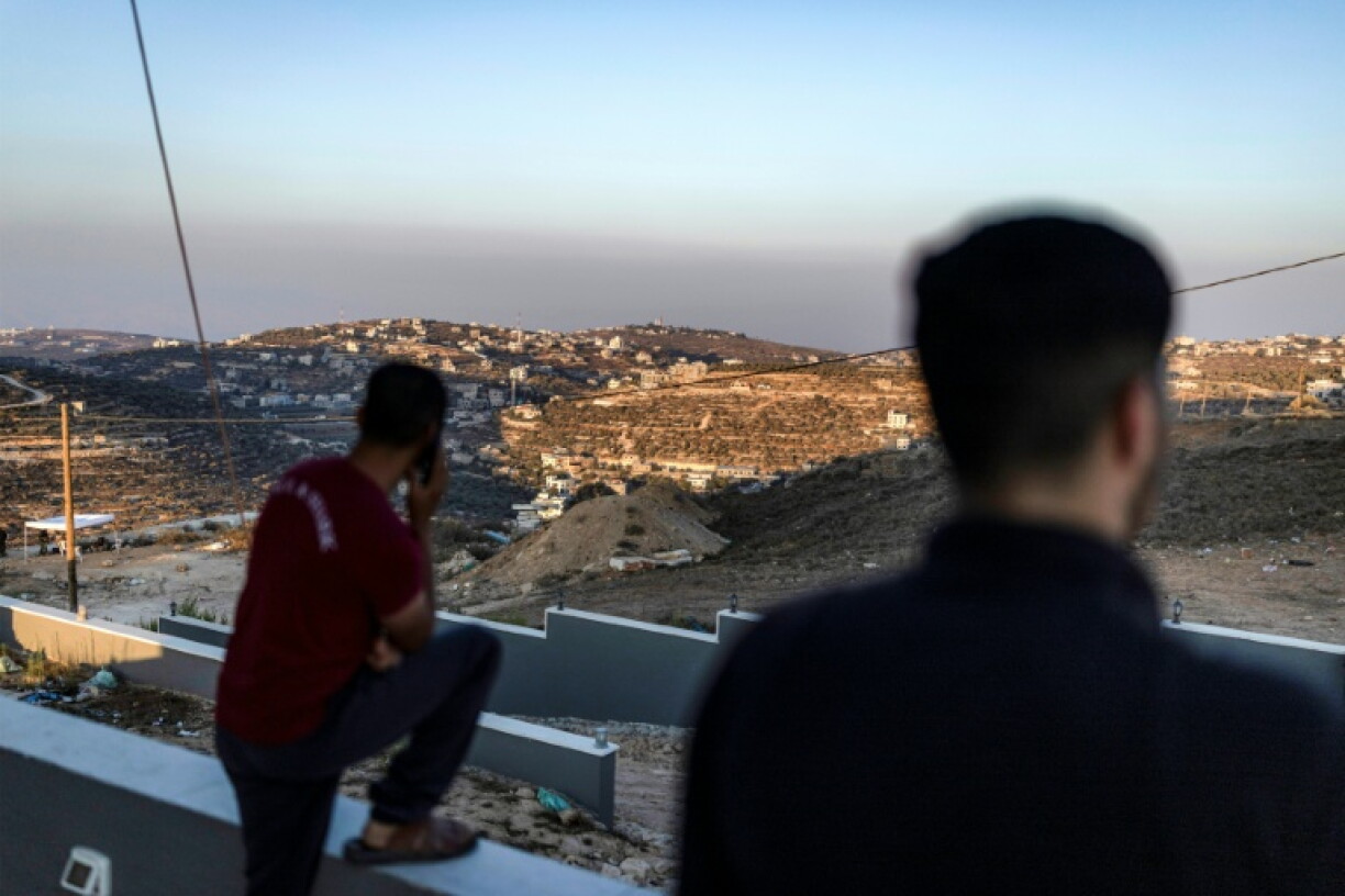 Des hommes palestiniens observent des soldats de l'armée israélienne depuis le toit d'une des maisons assiégées par des colons israéliens dans le village de Qusra, en Cisjordanie, le 18 août 2026