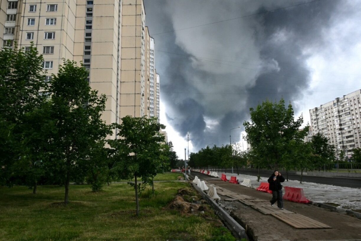 Une femme marche dans un quartier résidentiel tandis que de la fumée noire s'élève du site de la raffinerie russe de Gazprom Neft, située dans la banlieue sud-est de Moscou, le 18 juin 2026. L'Ukraine a mené tot le 18 juin une attaque de drones
