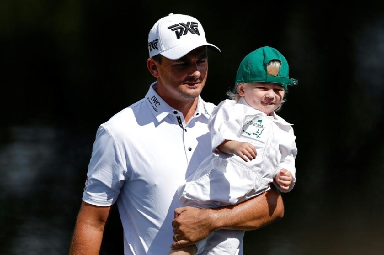 Christiaan Bezuidenhout of South Africa carries his son, John, during the Masters Par-Three Contest at Augusta National, where cricket legend A.B. de Villiers served as a caddie for him