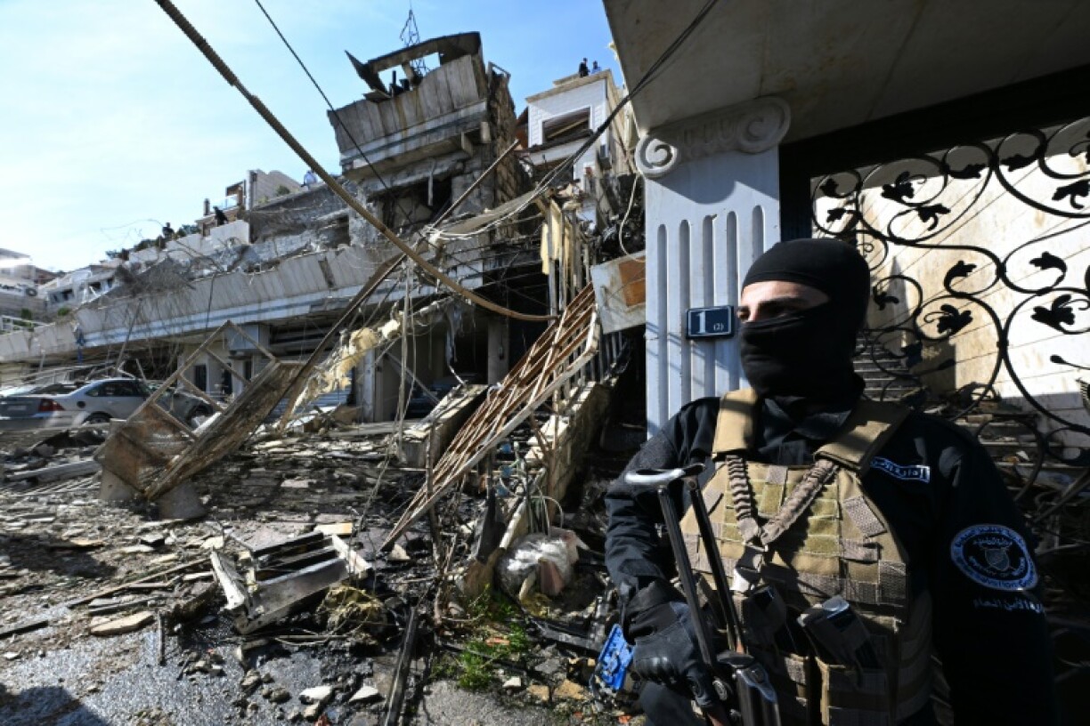 A member of the new Syrian administration's security forces stands guard at the site of an Israeli strike in a Damascus area where, a war monitor said, Palestinian leaders are known to reside