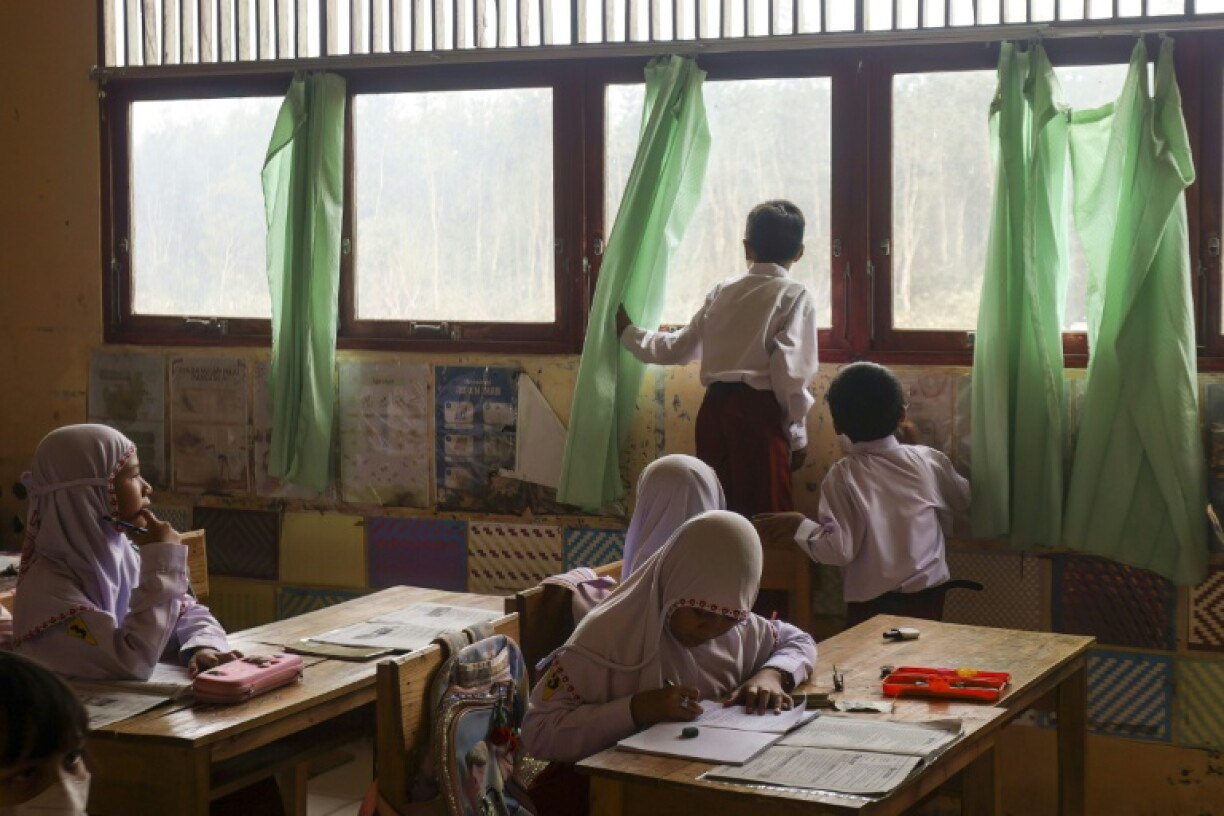 A child looks out of a classroom window before students at the elementary school were sent home early due to thick smoke from a land fire behind their school at Alalak village in Barito Kuala Regency, South Kalimantan on October 28, 2026. Toxic haze has covered parts of Indonesia, Malaysia and Singapore for weeks as Jakarta struggles to contain fires that have scorched large tracts of Borneo and Sumatra, with the smoke drifting across the region.