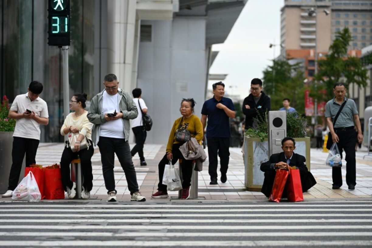 People wait to cross a street in a shopping area in Beijing. China's industrial production and retail sales growth slumped further last month, official data showed on September 15, missing forecasts and highlighting prolonged challenges in the world's second-largest economy