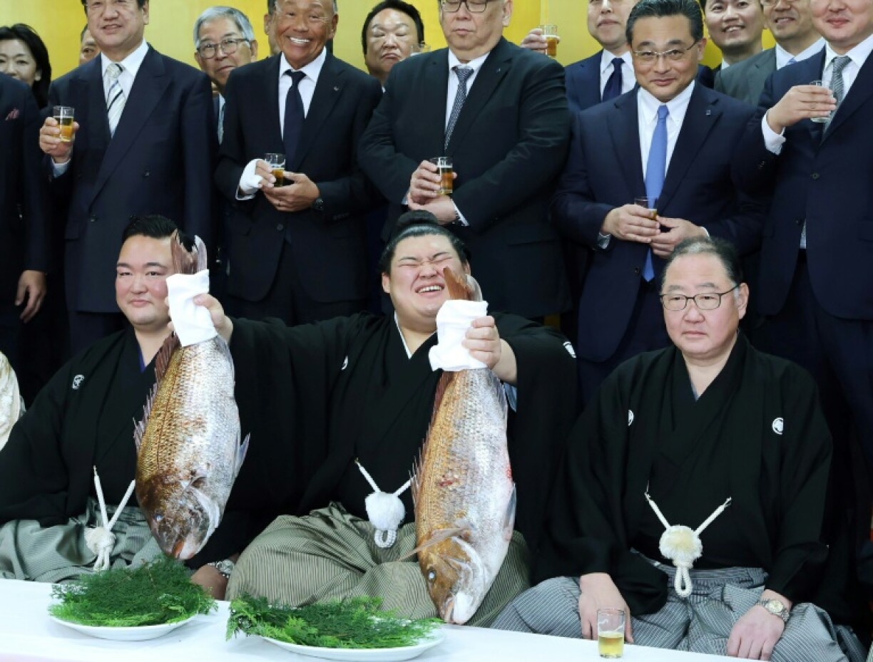 Onosato (centre) holds up a fish as to celebrate being promoted to sumo