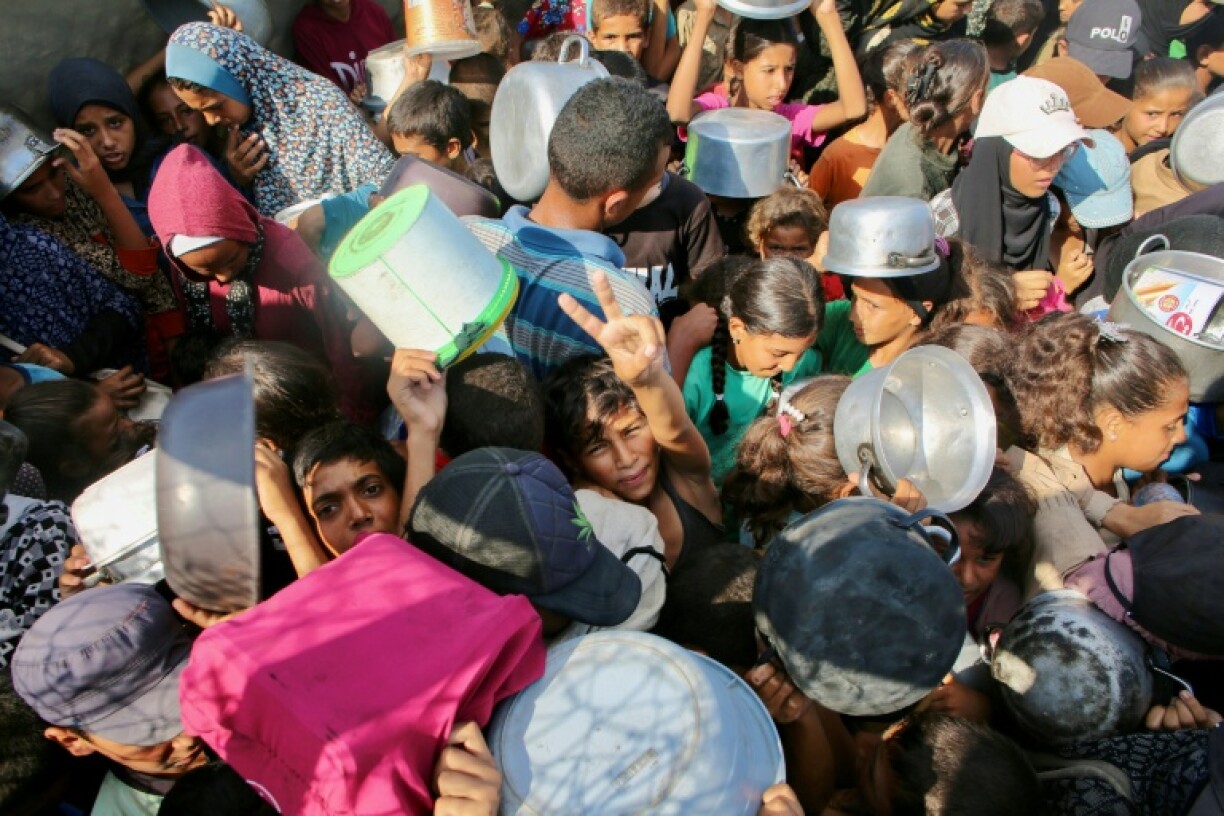 A Palestinian boy flashes the victory sign as he pushes through a crowd seeking a hot meal at a charity kitchen in the southern Gaza Strip