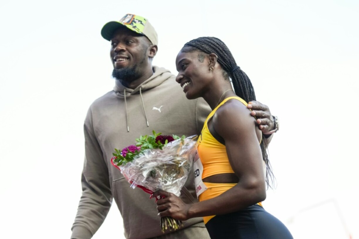 Jamaican sprint legend Usain Bolt presents a bouquet of flowers to Saint Lucia's Julien Alfred (R)