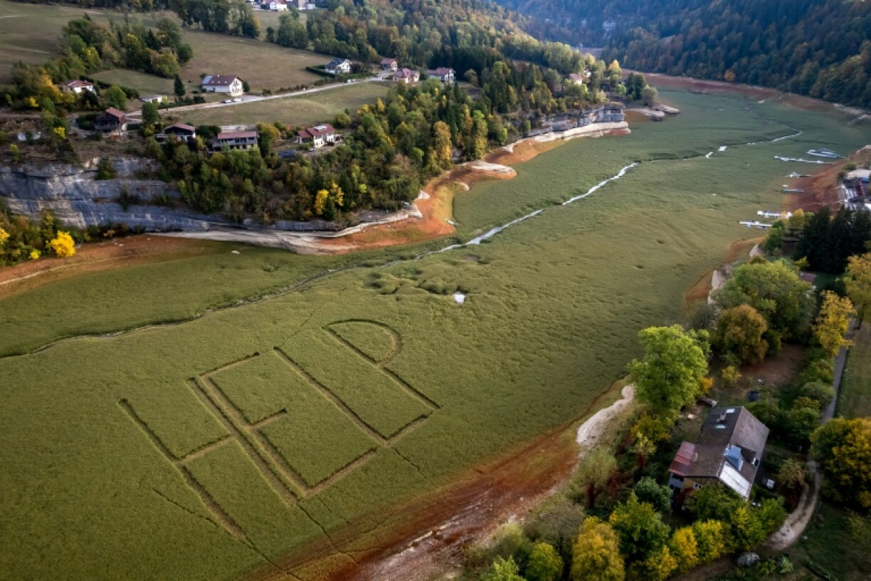 Cette photographie aérienne montre un gigantesque « Help » écrit par des habitants sur le lit herbeux de l’ancien lac asséché des Brenets (Lac des Brenets), partie du Doubs qui forme une frontière naturelle entre l’est de la France et l’ouest de la Suisse, aux Brenets, le 1er octobre 2026