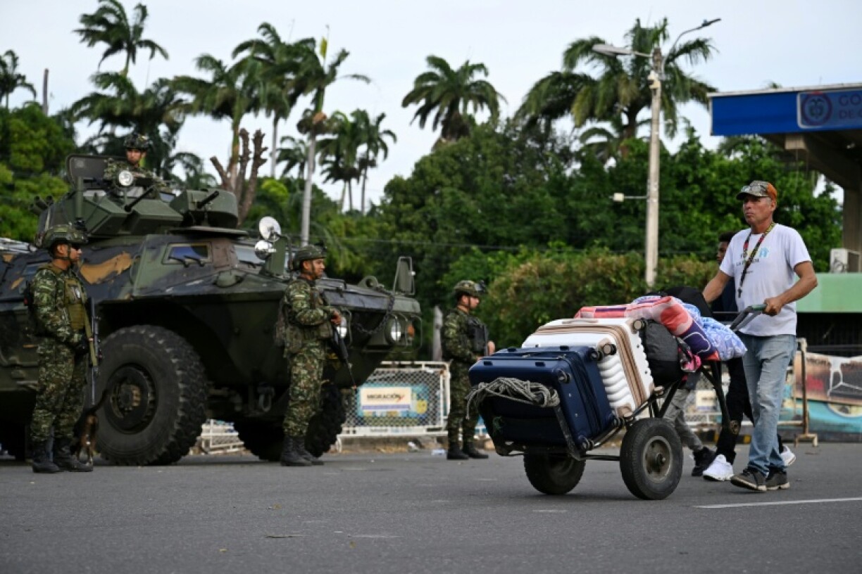 Un homme chargé de valises sur un diable passe devant des militaires colombiens stationnés à Cucuta, à la frontière avec le Venezuela, le 3 janvier 2026