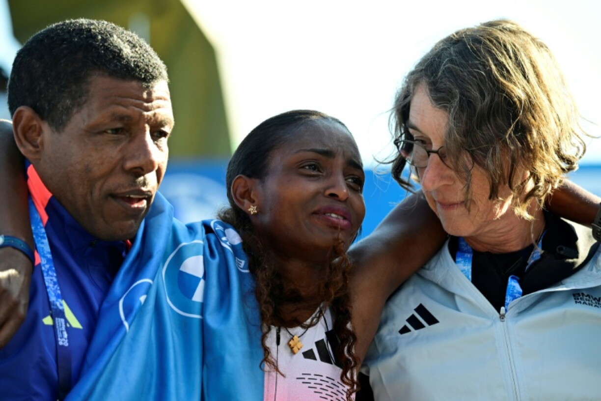 Ethiopia's Tigst Assefa (C) is helped off the track after crossing the finish line
