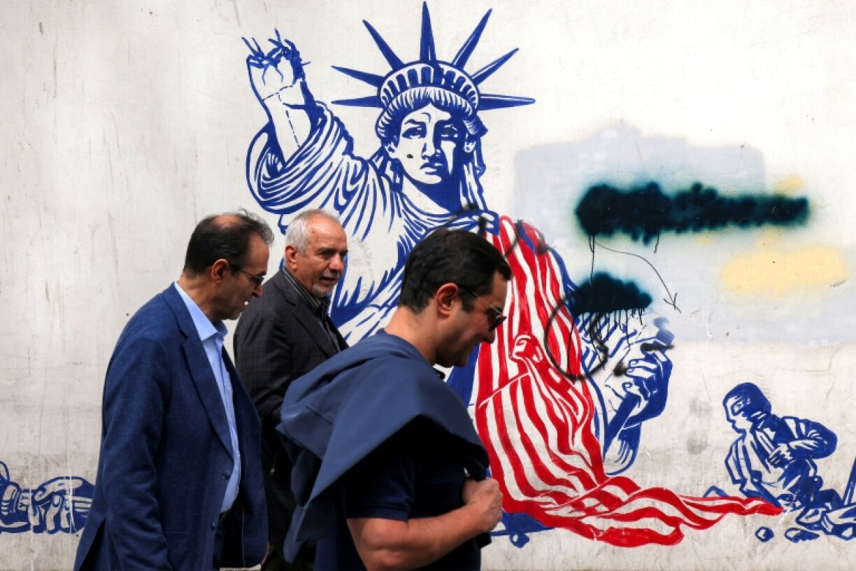 Iranian walk past a mural on the walls of the former US embassy building in Tehran, dubbed the