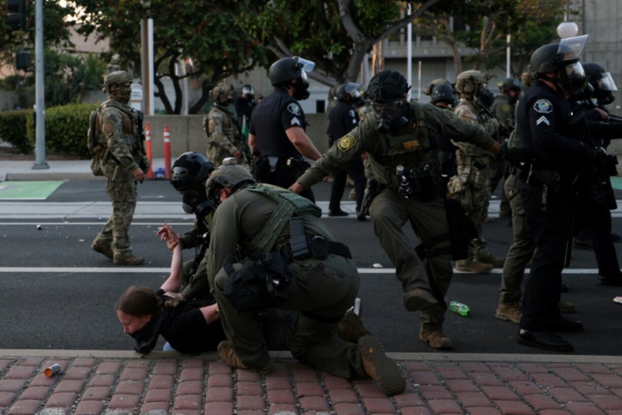 Des membres de la police des frontières plaquent au sol une manifestante à Santa Ana, en Californie, près du bureau des Services de l'Immigration, le 9 juin 2025, lors de protestations contre la politique migratoire de Donald Trump