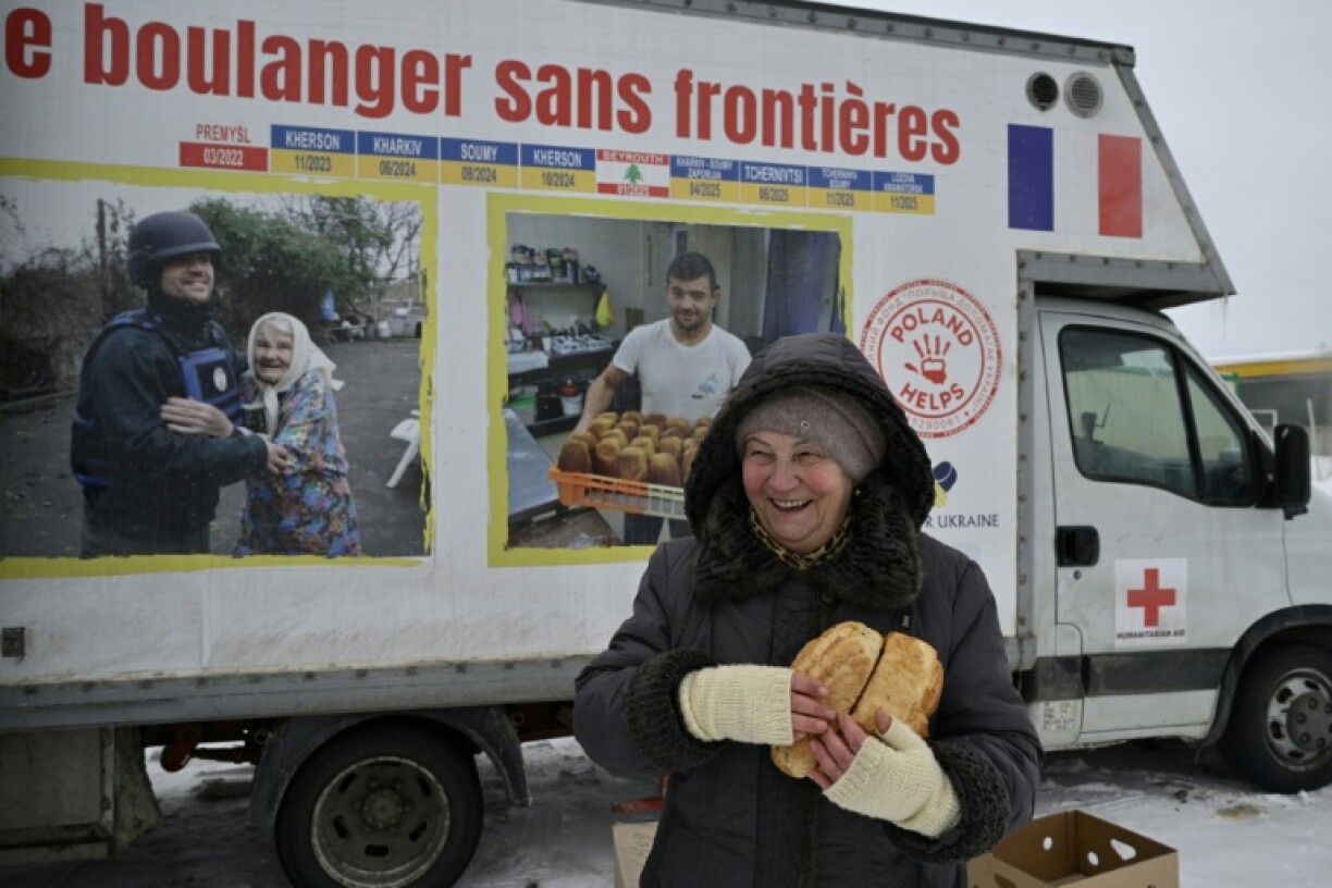Une femme réagit en tenant des pains fraîchement cuits distribués par le boulanger bénévole français Loïc Nervi depuis sa boulangerie mobile à Borodianka, dans la région de Kiev, le 19 février 2026, dans le contexte de l'invasion russe de l'Ukraine.