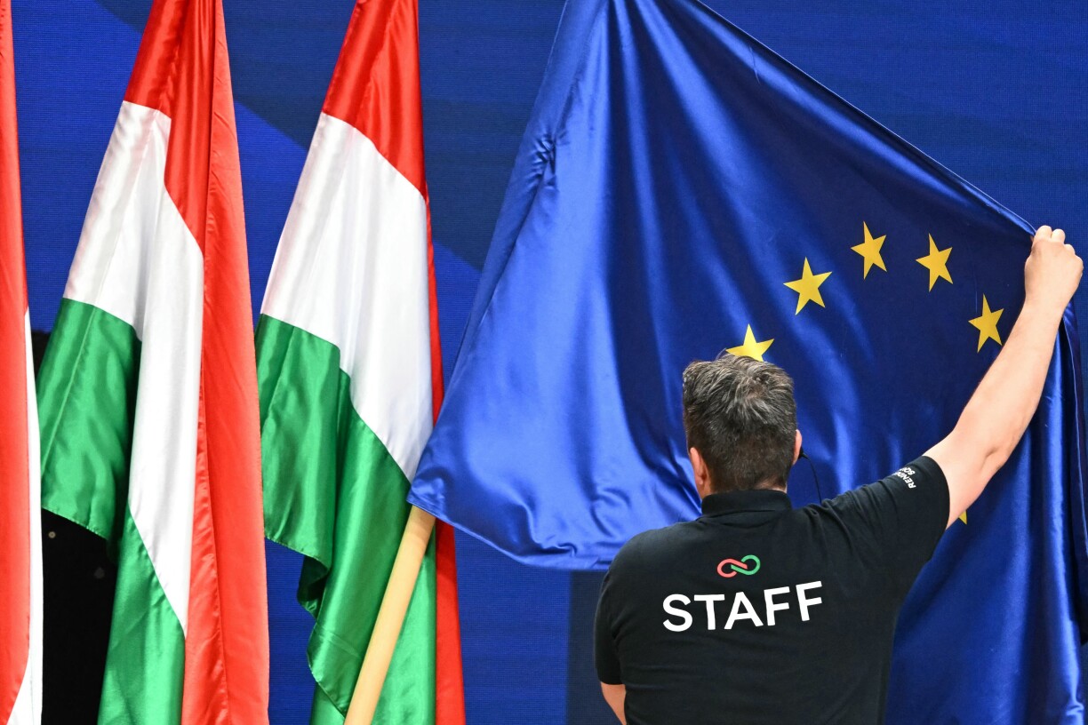 A staff member adjusts an EU-flag beside Hungarian flags at the HUNGEXPO Congress and Exhibition Center in Budapest, Hungary, on 13 April 2026.