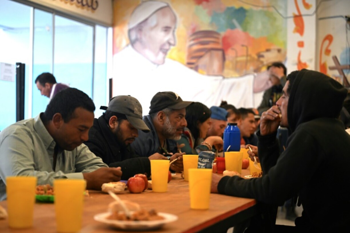 People eat next to a mural depicting Pope Francis at a community center for homeless drug addicts in Buenos Aires