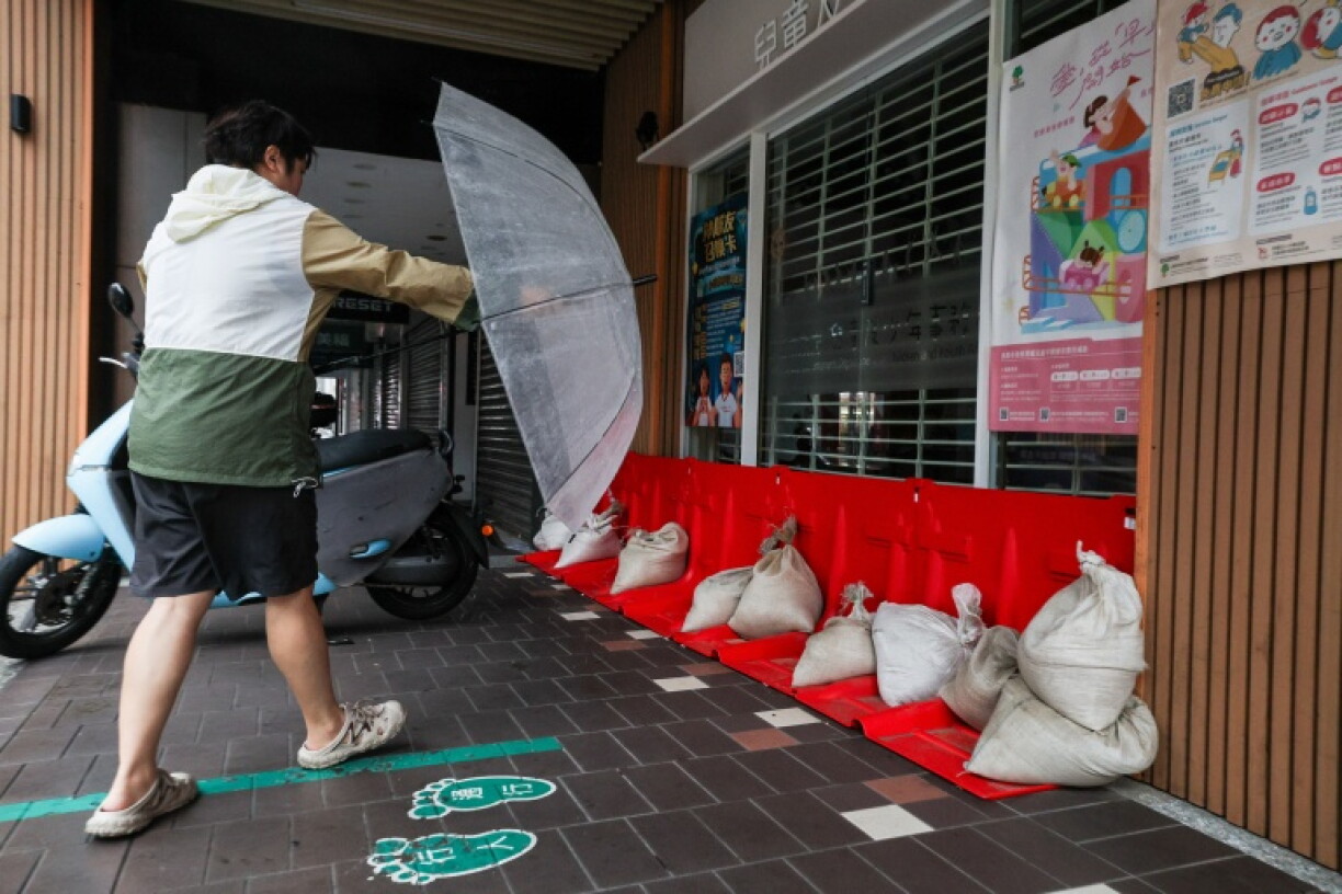 A pedestrian holding an umbrella walks past sandbags and flood barriers placed outside a building as Typhoon Champi approaches